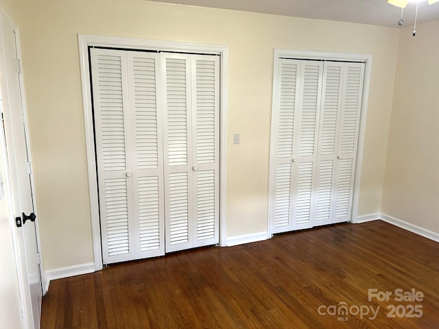 unfurnished bedroom with baseboards, multiple closets, and dark wood-style floors