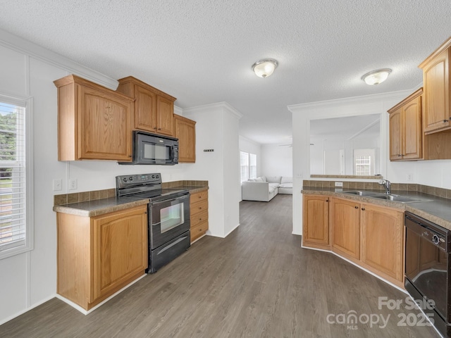 kitchen with a sink, dark countertops, black appliances, and dark wood-type flooring