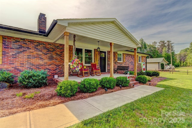 exterior space featuring covered porch, brick siding, a yard, and a chimney