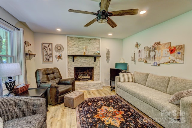 living room featuring recessed lighting, a ceiling fan, light wood finished floors, and a stone fireplace