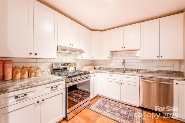 4805 Nesbit Rd, Monroe, NC 28112 - kitchen featuring backsplash, a sink, under cabinet range hood, stainless steel appliances, and white cabinetry