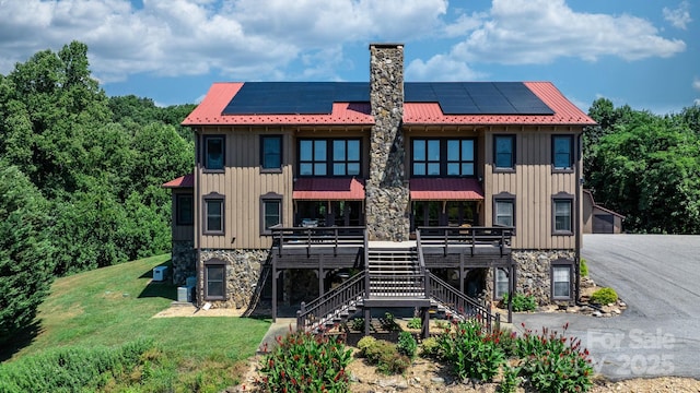 back of house featuring board and batten siding, a chimney, stairway, roof mounted solar panels, and stone siding