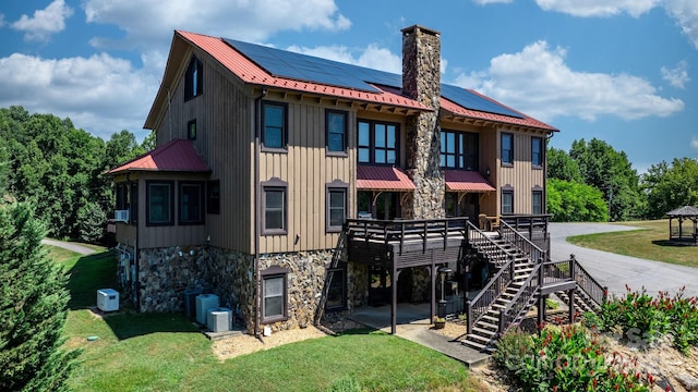 rear view of property featuring stairway, a lawn, solar panels, and stone siding