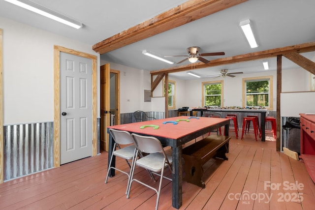 dining area with light wood-style floors, a ceiling fan, and beamed ceiling