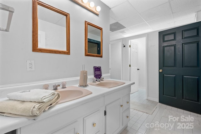 bathroom with a sink, tile patterned flooring, a drop ceiling, and double vanity