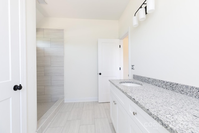 bathroom with baseboards, vanity, and tiled shower