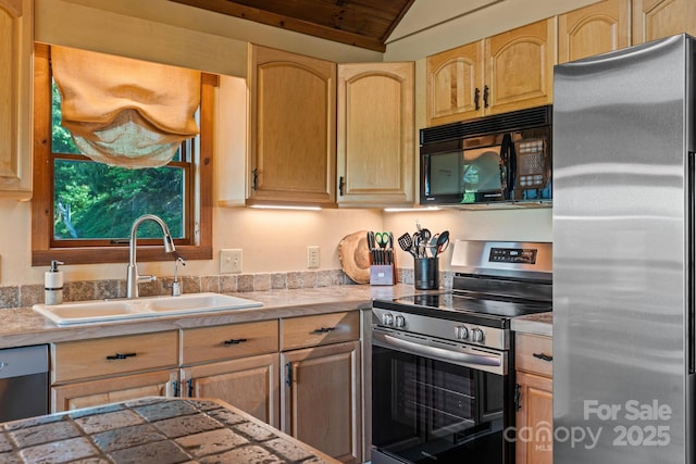 kitchen with light brown cabinetry, appliances with stainless steel finishes, vaulted ceiling, and a sink