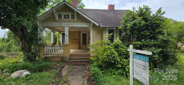 view of front of home featuring a porch, roof with shingles, and a chimney