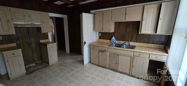 kitchen with wood walls, range hood, light countertops, a sink, and light tile patterned floors