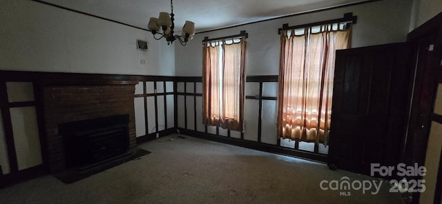 unfurnished living room with visible vents, carpet, a brick fireplace, and a notable chandelier