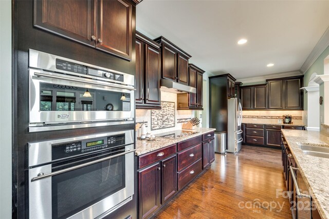 308 Hollister Estates Dr, Waxhaw, NC 28173 - kitchen with appliances with stainless steel finishes, backsplash, under cabinet range hood, light stone counters, and wood finished floors