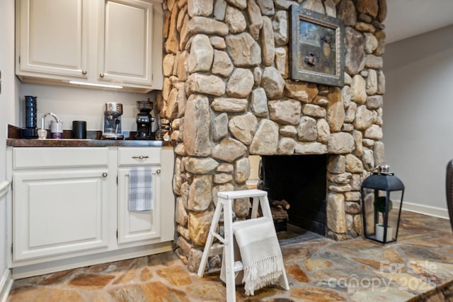 bar with wet bar, stone finish flooring, a stone fireplace, and baseboards