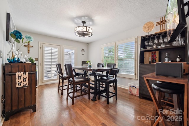 dining room featuring baseboards, a textured ceiling, and wood finished floors