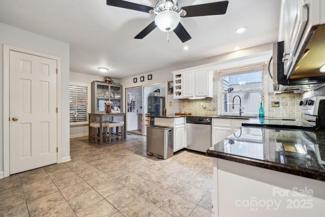 kitchen featuring decorative backsplash, dark countertops, white cabinetry, a sink, and dishwasher