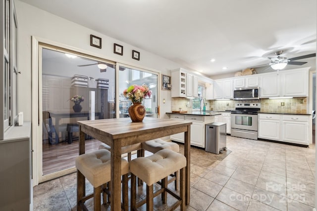 kitchen with white cabinets, ceiling fan, appliances with stainless steel finishes, dark countertops, and backsplash