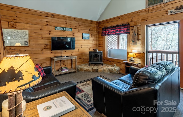 carpeted living area featuring a wood stove, wood walls, and lofted ceiling