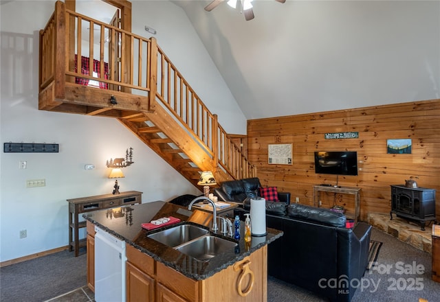 kitchen featuring a sink, a wood stove, ceiling fan, dark colored carpet, and white dishwasher