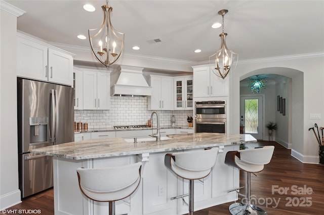 kitchen with custom range hood, arched walkways, appliances with stainless steel finishes, and a notable chandelier