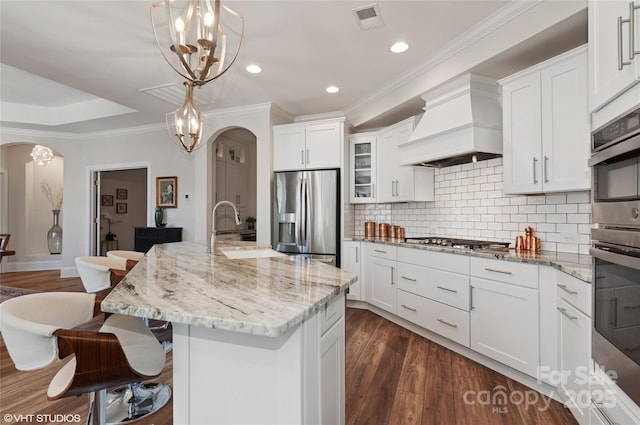 kitchen featuring backsplash, appliances with stainless steel finishes, arched walkways, a breakfast bar, and custom range hood