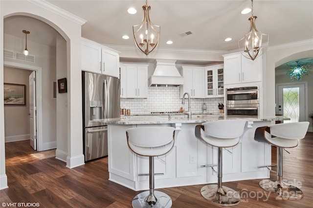 kitchen featuring visible vents, arched walkways, premium range hood, a notable chandelier, and stainless steel appliances