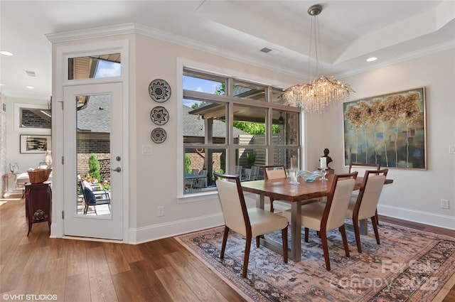 dining space featuring visible vents, hardwood / wood-style flooring, baseboards, a notable chandelier, and a tray ceiling