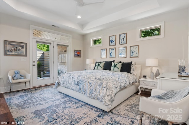 bedroom with wood finished floors, a raised ceiling, baseboards, access to outside, and recessed lighting