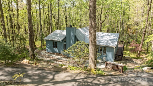 view of front of house with a view of trees, a chimney, and metal roof
