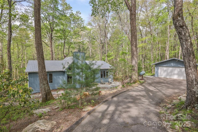 ranch-style house featuring a garage, an outbuilding, a chimney, and a forest view