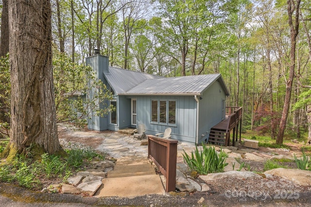 view of front of property featuring a wooden deck, stairs, a chimney, and metal roof