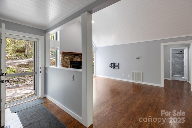 entrance foyer with visible vents, lofted ceiling, wood finished floors, baseboards, and a stone fireplace