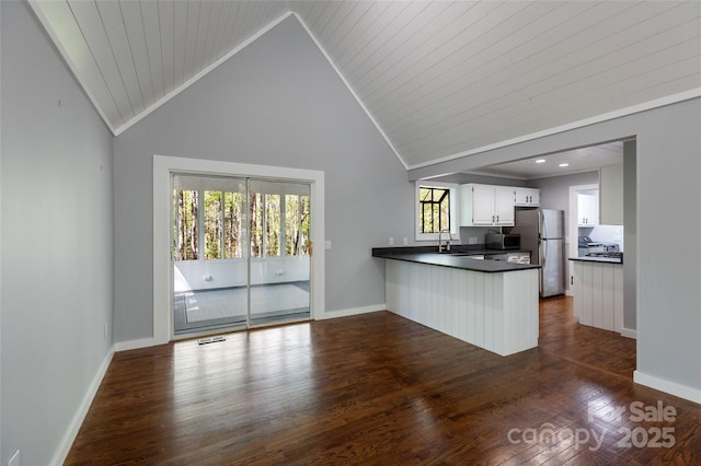 kitchen with dark countertops, appliances with stainless steel finishes, a sink, dark wood finished floors, and a peninsula