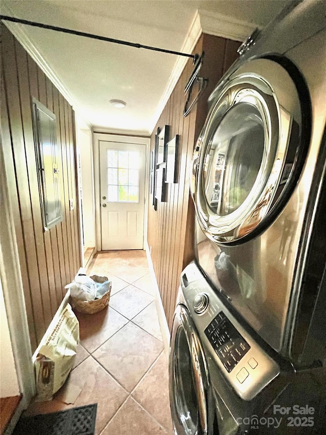 clothes washing area featuring crown molding, stacked washing maching and dryer, wood walls, and laundry area