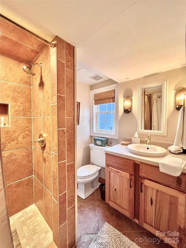 bathroom featuring toilet, a tile shower, visible vents, tile patterned flooring, and vanity