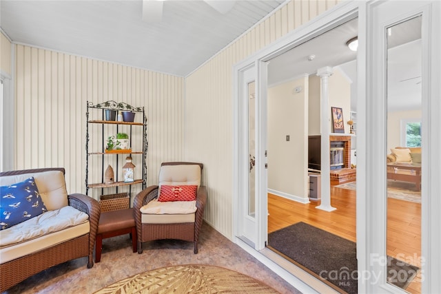 living area featuring ornate columns, wallpapered walls, a ceiling fan, wood finished floors, and baseboards