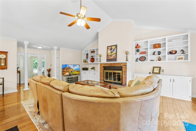 living area with vaulted ceiling, light wood-style floors, a ceiling fan, a brick fireplace, and built in features