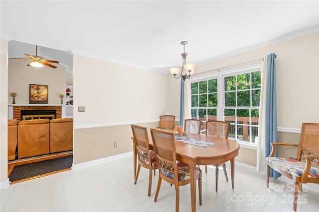 dining room featuring baseboards, a ceiling fan, a chandelier, and a brick fireplace