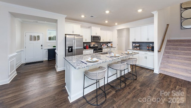 kitchen with appliances with stainless steel finishes, a sink, an island with sink, dark wood-type flooring, and visible vents