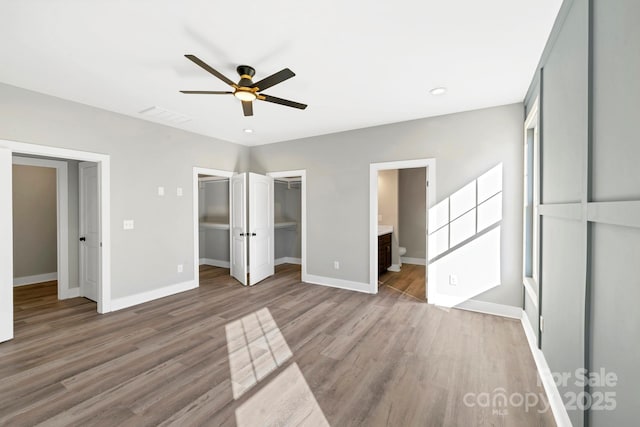 unfurnished bedroom with visible vents, wood finished floors, baseboards, a spacious closet, and ensuite bath