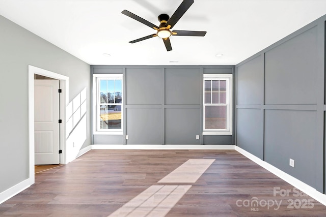 spare room featuring wood finished floors, a ceiling fan, baseboards, and a decorative wall