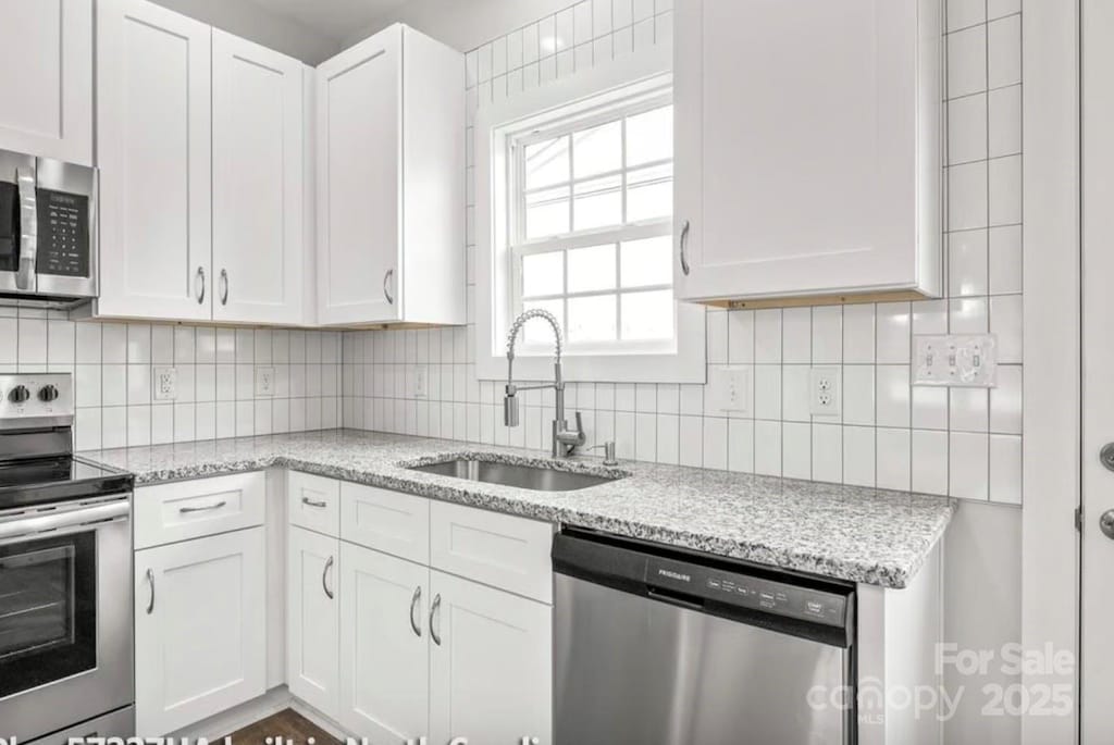 kitchen with white cabinets, appliances with stainless steel finishes, a sink, and tasteful backsplash