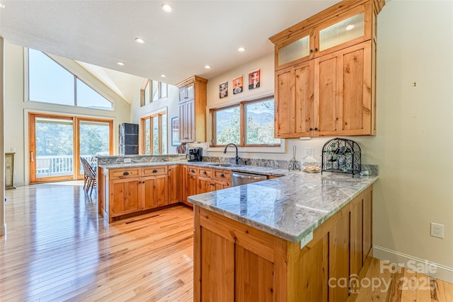 kitchen featuring a peninsula, glass insert cabinets, light wood-style flooring, a sink, and light stone counters