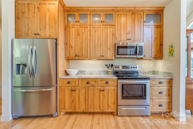 kitchen with light wood finished floors, appliances with stainless steel finishes, and glass insert cabinets