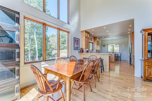 dining space with light wood-style flooring, a high ceiling, baseboards, and recessed lighting