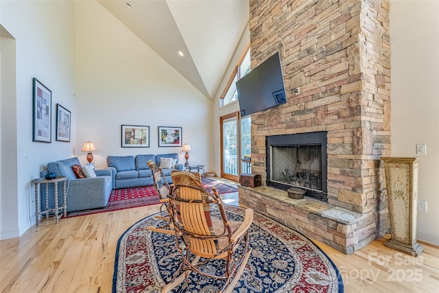 living area featuring baseboards, a stone fireplace, hardwood / wood-style floors, and high vaulted ceiling