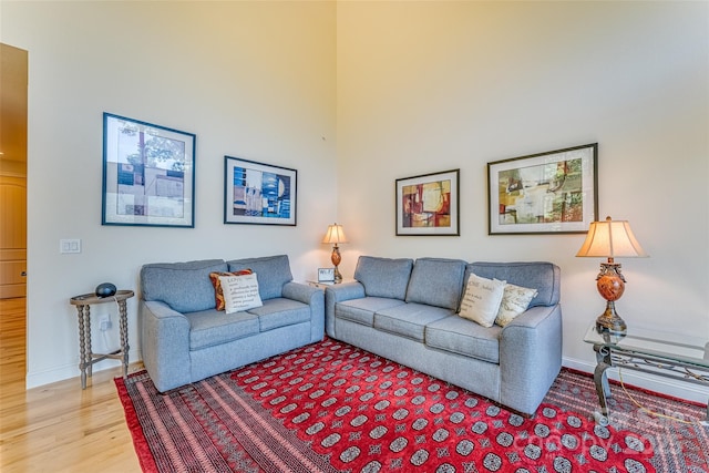 living area with baseboards, light wood-style floors, and a towering ceiling