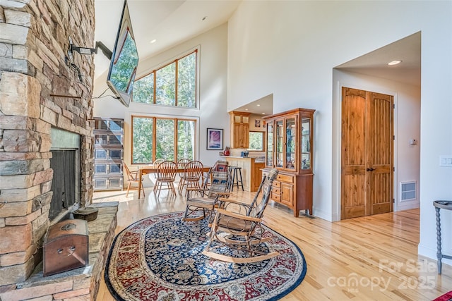 living area featuring wood finished floors, a high ceiling, visible vents, baseboards, and a stone fireplace