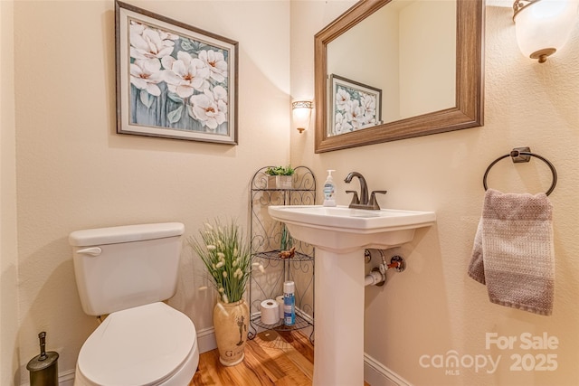 half bath with toilet, wood finished floors, baseboards, and a sink