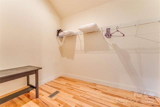 walk in closet with lofted ceiling, visible vents, and wood finished floors