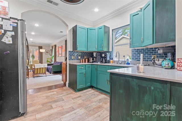 kitchen featuring freestanding refrigerator, arched walkways, a healthy amount of sunlight, and light wood-style floors