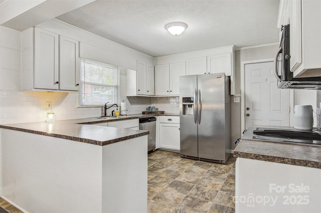kitchen featuring dark countertops, appliances with stainless steel finishes, a sink, a peninsula, and tasteful backsplash